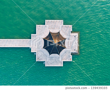 Aerial top down view of unique hexagonal pavilion at the end of a long white pier extending into vibrant green water Aerial top down view of unique hexagonal pavilion at the end of a long white pier extending into vibrant green water 139439103