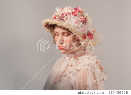 Young woman models elaborate flower hat and vintage-inspired sheer top in a bright studio Young woman models elaborate flower hat and vintage-inspired sheer top in a bright studio 139439336