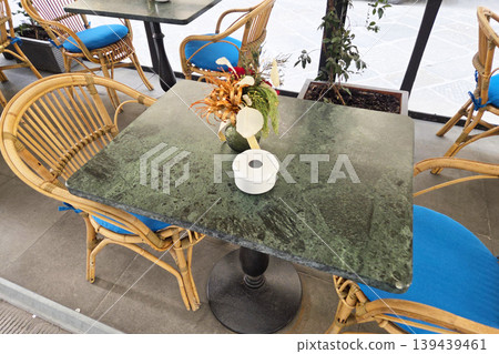 Cozy Outdoor Cafe Seating with Rattan Chairs and Floral Arrangement for Relaxed Dining Cozy Outdoor Cafe Seating with Rattan Chairs and Floral Arrangement for Relaxed Dining 139439461