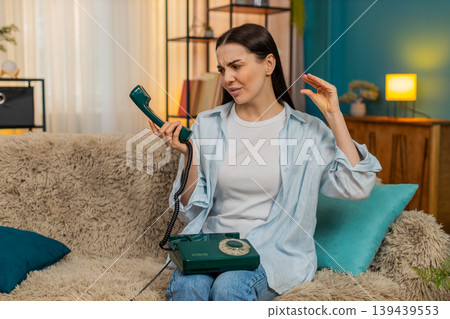 Young woman talking on retro 90s telephone making funny faces unwilling annoyed conversation mood Young woman talking on retro 90s telephone making funny faces unwilling annoyed conversation mood 139439553