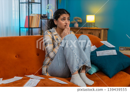 Indian woman praying sitting on sofa looking upward asking help holding documents hoping for miracle Indian woman praying sitting on sofa looking upward asking help holding documents hoping for miracle 139439555