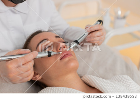 Caucasian young woman gets lips zone facial therapy with modern device by cosmetologist in clinic 139439558