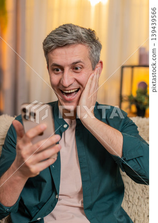 Smiling man celebrates smartphone victory with clenched fist, joyfully reacting to good result 139439566