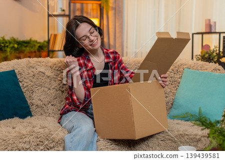 Woman unpacking delivery box at home, smiling with satisfaction while checking new items with joy Woman unpacking delivery box at home, smiling with satisfaction while checking new items with joy 139439581