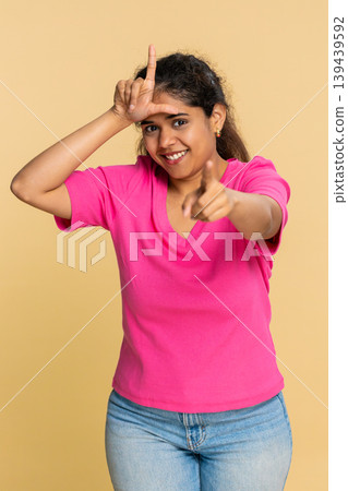 Indian woman making L loser sign on forehead, smiling ironically, humorously teasing someone 139439592