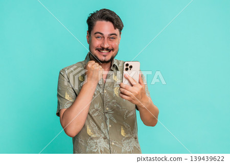 Adult man clenches fist with joy while looking at smartphone celebrating victory good news reaction Adult man clenches fist with joy while looking at smartphone celebrating victory good news reaction 139439622