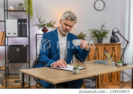 Middle-aged businessman stretches enjoys aromatic coffee sip squints satisfied and resumes paperwork Middle-aged businessman stretches enjoys aromatic coffee sip squints satisfied and resumes paperwork 139439653