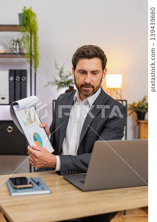 Middle-aged businessman hosts webinar on laptop camera gestures with energy and shows clear charts Middle-aged businessman hosts webinar on laptop camera gestures with energy and shows clear charts 139439660