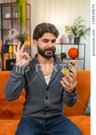 Indian man confirms online purchase with smartphone and card enters cvv nods relief approval gesture 139439678
