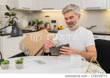 Middle-aged man counts cash sets aside money for bills puts rest in wallet satisfied control gesture 139439771