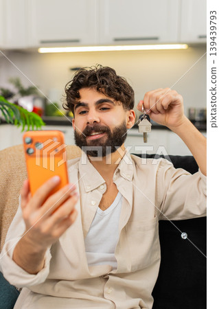 Indian man smartphone video call smiling showing apartment keys to family celebrating new life start Indian man smartphone video call smiling showing apartment keys to family celebrating new life start 139439793