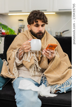 Indian man under blanket using smartphone reading doctor advice and health tips while feeling sick 139439795