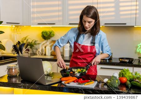 Young woman cooking vegetables with laptop recipe in modern home kitchen for healthy diet meal prep Young woman cooking vegetables with laptop recipe in modern home kitchen for healthy diet meal prep 139439867