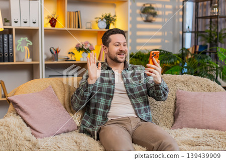 Young man on home sofa greeting smartphone camera with ok gesture and friendly smile for video story Young man on home sofa greeting smartphone camera with ok gesture and friendly smile for video story 139439909