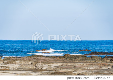平坦的岩石海岸線,藍色的海水和白色的波浪形成了鮮明的對比。 平坦的岩石海岸線,藍色的海水和白色的波浪形成了鮮明的對比。 139440236