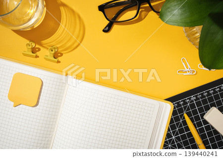 Open notebook on yellow background with glasses, pen, and office supplies. Workspace for planning or business, copy space. 139440241