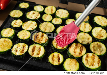 Applying Sauce to Roasted Zucchini Rounds on Electric Contact Grill. Applying Sauce to Roasted Zucchini Rounds on Electric Contact Grill. 139440304
