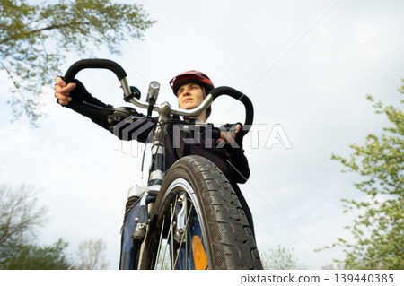 Confident young woman cyclist holding handlebars and looking into the distance Confident young woman cyclist holding handlebars and looking into the distance 139440385