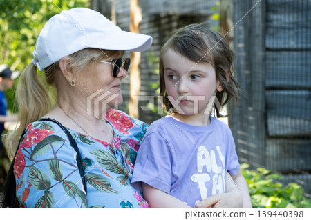Senior woman in white cap and sunglasses holding grandson in park Senior woman in white cap and sunglasses holding grandson in park 139440398