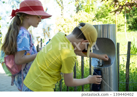 Children filling reusable water bottles from drinking fountain in park Children filling reusable water bottles from drinking fountain in park 139440402