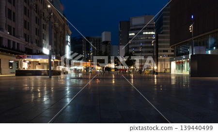 A city square at night; wet pavement and reflections of buildings; deserted cityscape; night view. A city square at night; wet pavement and reflections of buildings; deserted cityscape; night view. 139440499