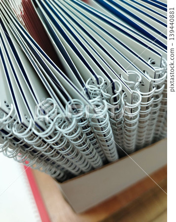 Stack of spiral-bound notebooks with white covers and colorful edges arranged neatly in a cardboard box on a wooden surface Stack of spiral-bound notebooks with white covers and colorful edges arranged neatly in a cardboard box on a wooden surface 139440881