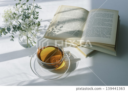 Morning light, tea, a book, and a peaceful reading time with white flowers. 139441363