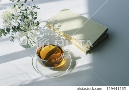 A quiet time with morning light, tea, a book, and white flowers. 139441365
