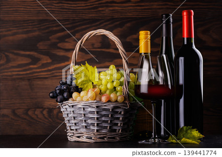 Red and white wine bottles with a glass and basket of fresh grapes 139441774