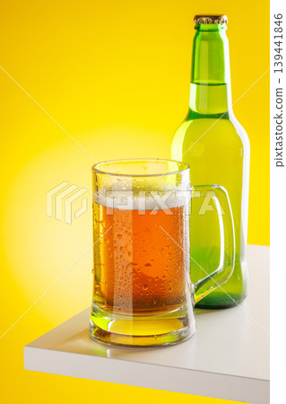 Beer mug with foam and bottle on yellow background snack setup Beer mug with foam and bottle on yellow background snack setup 139441846