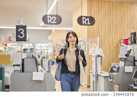 一位年輕女子在自助結帳機付款後，將環保袋挎在肩上。 139441878