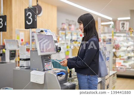 一位年輕女子正在使用智慧型手機在自助結帳櫃檯付款。 一位年輕女子正在使用智慧型手機在自助結帳櫃檯付款。 139441880