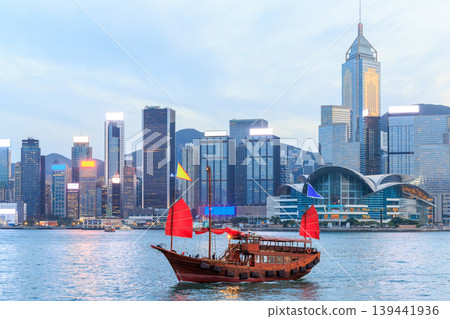 Traditional wooden junk boat with red sails against Hong Kong skyline during sunset Traditional wooden junk boat with red sails against Hong Kong skyline during sunset 139441936
