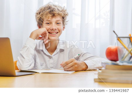 Schoolboy studying at home with a laptop, smiling with a joyful expression 139441987