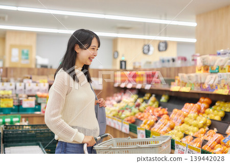 一位年輕女子在超市購物時一邊看著她的智慧型手機。 139442028