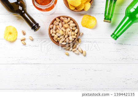 Beer bottles with pistachios and chips on white table 139442135