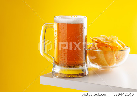 Beer mug with foam and chips on yellow background snack setup Beer mug with foam and chips on yellow background snack setup 139442140