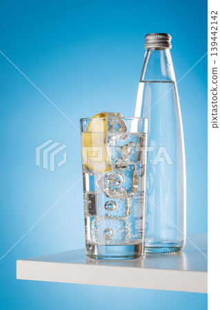 Sparkling water with lemon and bottle on blue background refreshment Sparkling water with lemon and bottle on blue background refreshment 139442142