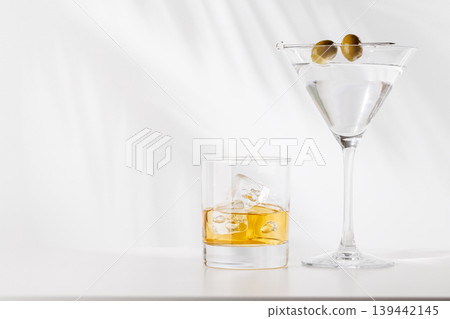 Glass of whiskey with ice and martini with olives on white background Glass of whiskey with ice and martini with olives on white background 139442145