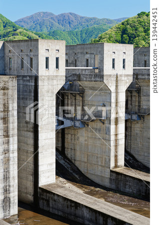 A large concrete dam structure with mountains in the background. A large concrete dam structure with mountains in the background. 139442451