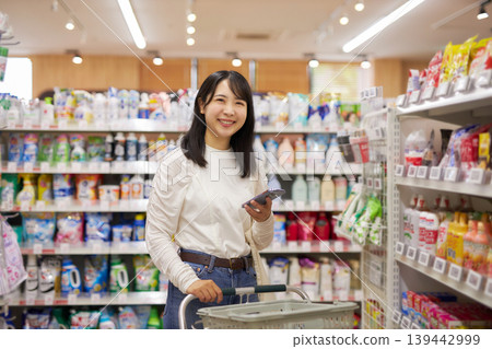A young woman shopping at a supermarket while looking at notes on her smartphone. A young woman shopping at a supermarket while looking at notes on her smartphone. 139442999