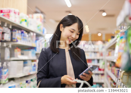 一位女商人一邊在超市購物,一邊用智慧型手機查看筆記。 一位女商人一邊在超市購物,一邊用智慧型手機查看筆記。 139443021