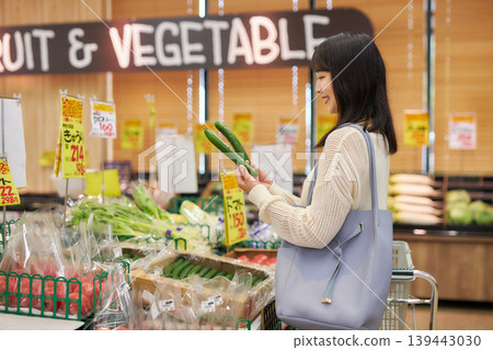 A young woman shopping at a supermarket while looking at her smartphone. A young woman shopping at a supermarket while looking at her smartphone. 139443030