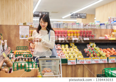 A young woman shopping at a supermarket while looking at her smartphone. A young woman shopping at a supermarket while looking at her smartphone. 139443033