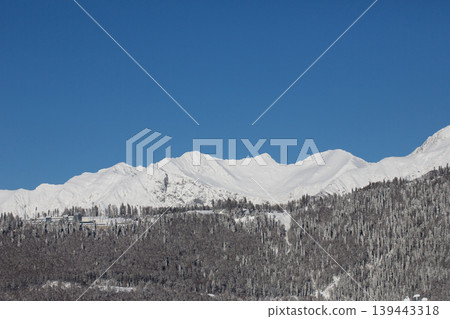 View of the mountains from Rosa Khutor, Krasnaya Polyana in winter. Snow-covered mountains against a blue sky. View of the mountains from Rosa Khutor, Krasnaya Polyana in winter. Snow-covered mountains against a blue sky. 139443318