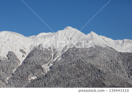 View of the mountains from Rosa Khutor, Krasnaya Polyana in winter. Snow-covered mountains against a blue sky. 139443328