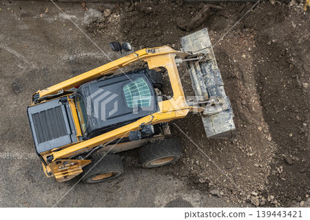 A skid steer loader shovels soil in a park. Construction heavy equipment for earthworks A skid steer loader shovels soil in a park. Construction heavy equipment for earthworks 139443421