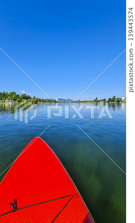Red paddleboard in the middle of a calm river under a clear blue sky. Summer water sport, mental vitality, burst of energy. 139443574