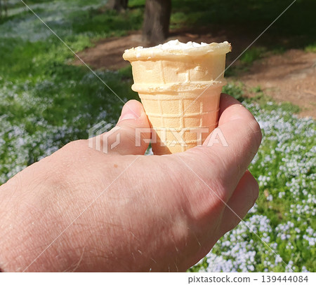 A man's hand holds a waffle cup with white ice cream against the background of a bright spring meadow A man's hand holds a waffle cup with white ice cream against the background of a bright spring meadow 139444084