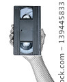 Hand holding a VHS video cassette isolated on transparent background with vintage newspaper print texture. Concept of retro media, analog video technology and nostalgic communication 139445833